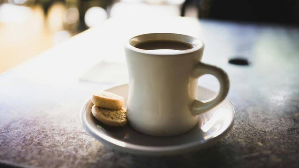 A cup of coffee on a saucer with two cookies.