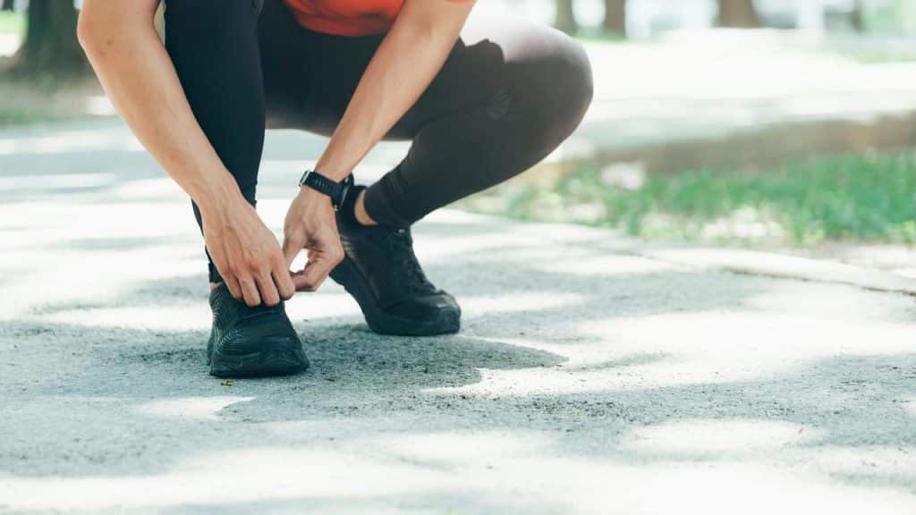 A person tying shoelaces on a running path.
