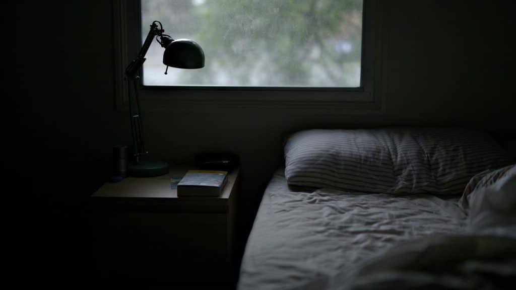 A dimly lit bedroom with an unmade bed and a nightstand
