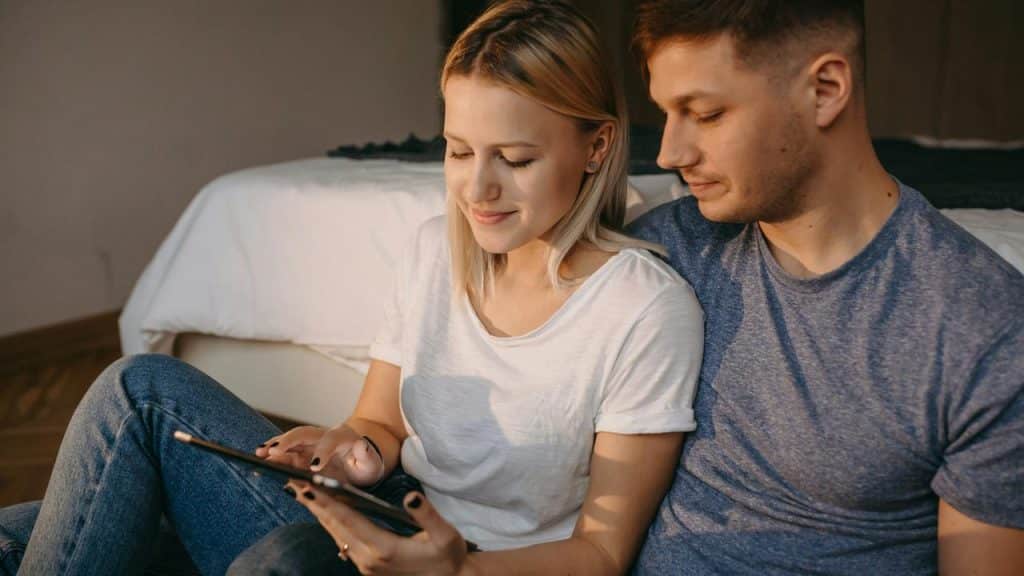 A couple sitting on the floor using a tablet together.