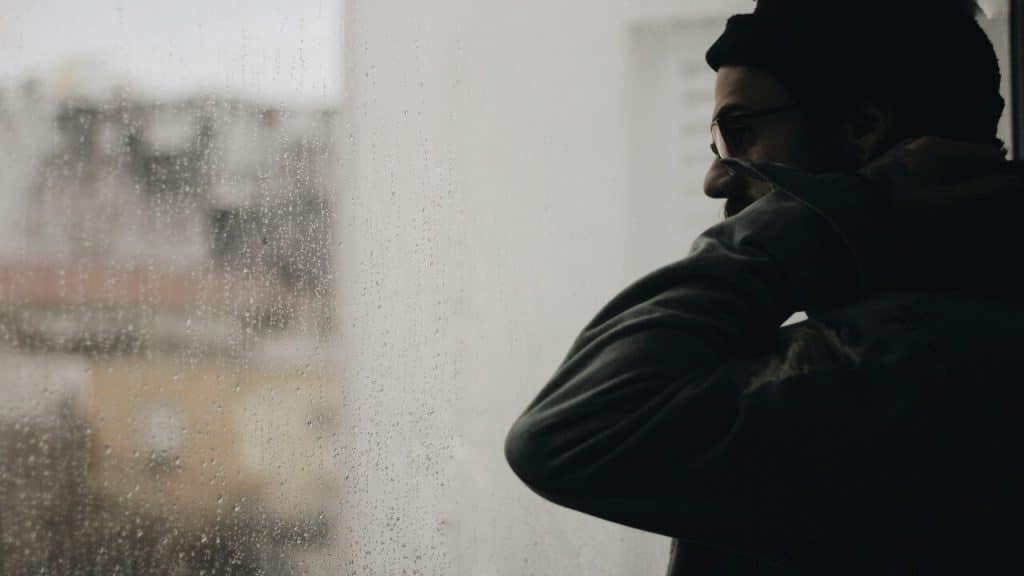 A man looking out the glass window during the rain.