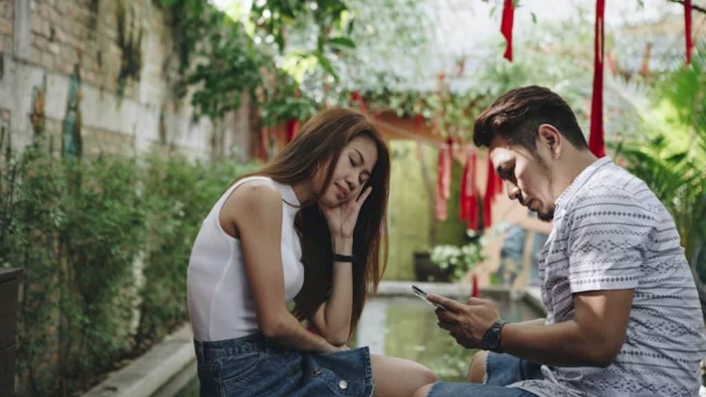 Man texting on phone while woman waits with disappointment.