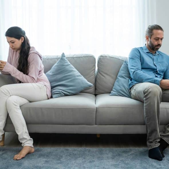 A man and woman sitting away from each other at the couch.
