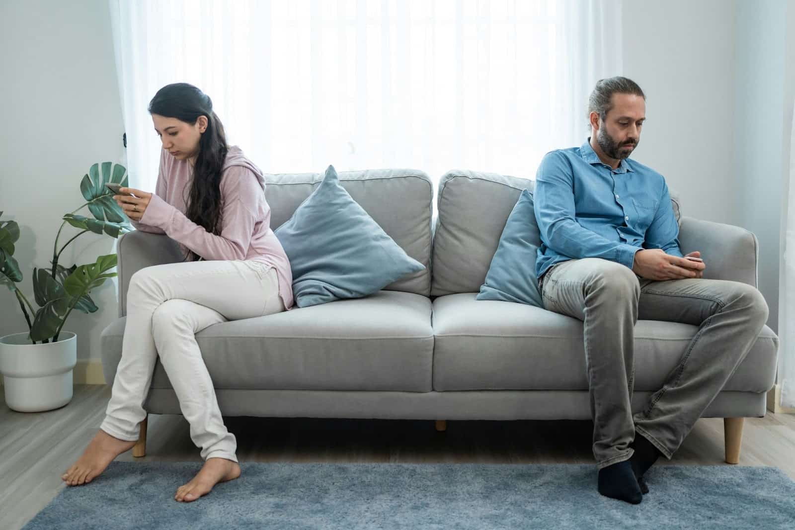 A man and woman sitting away from each other at the couch.