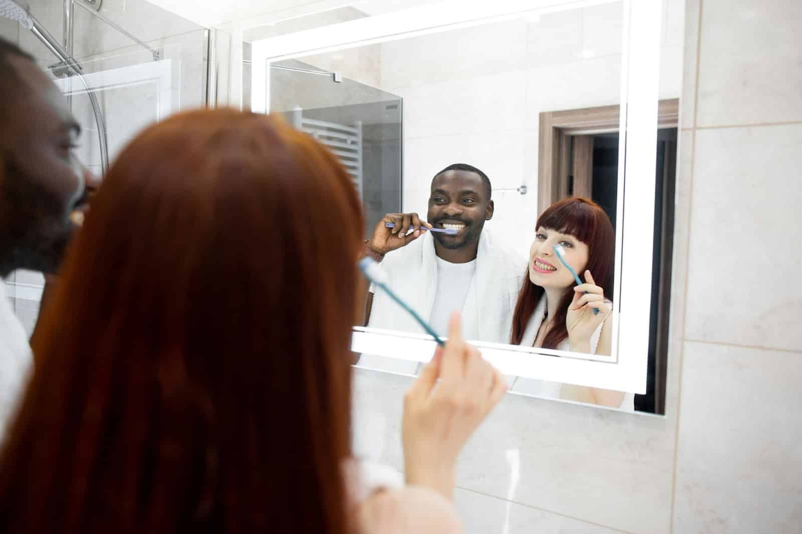 A man and woman at the bathroom brushing teeth.