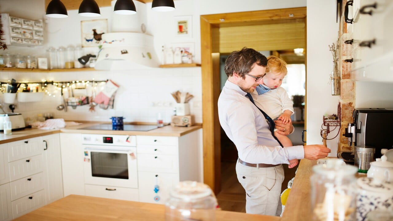 A man carrying his son in the kitchen.
