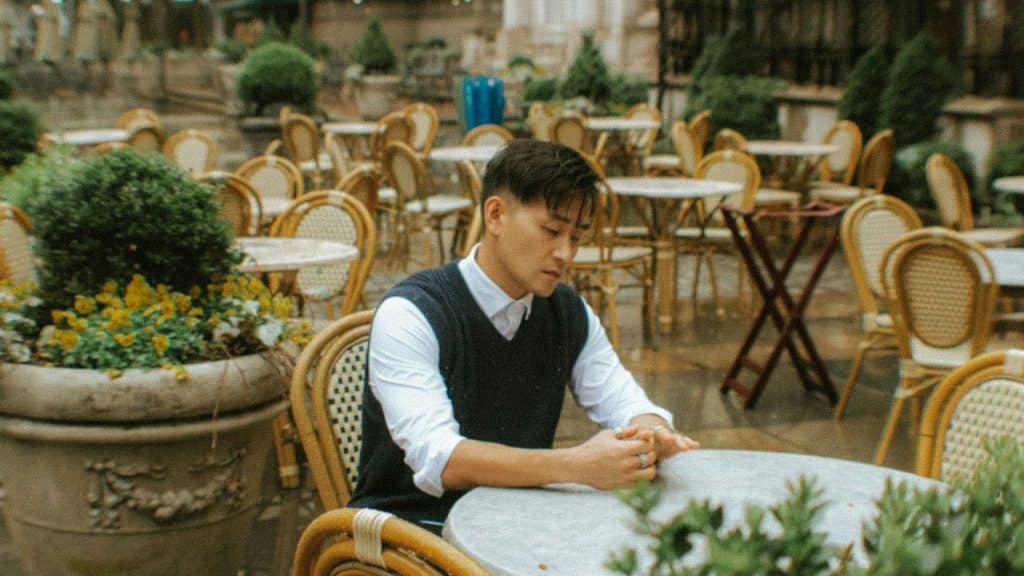 A man in a vest and white shirt sits alone at an outdoor cafe table.