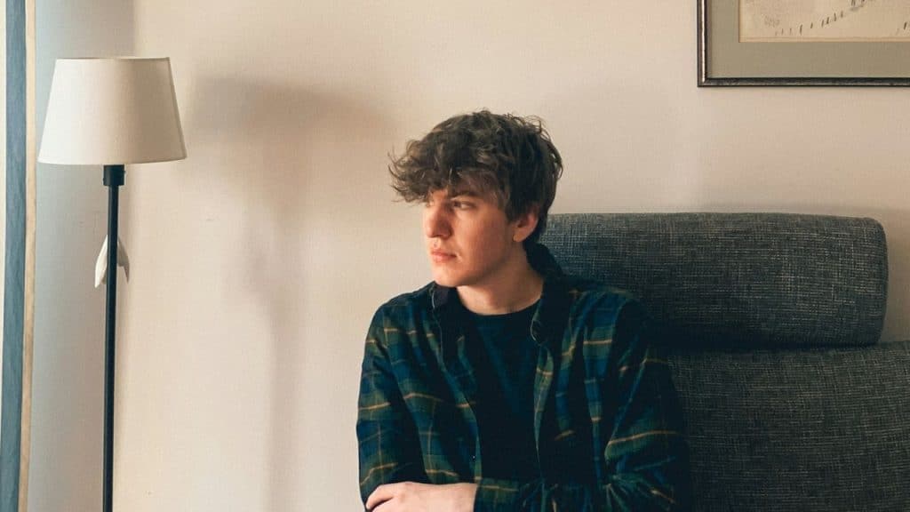 A person with curly hair and a plaid shirt sits, looking away from the camera.