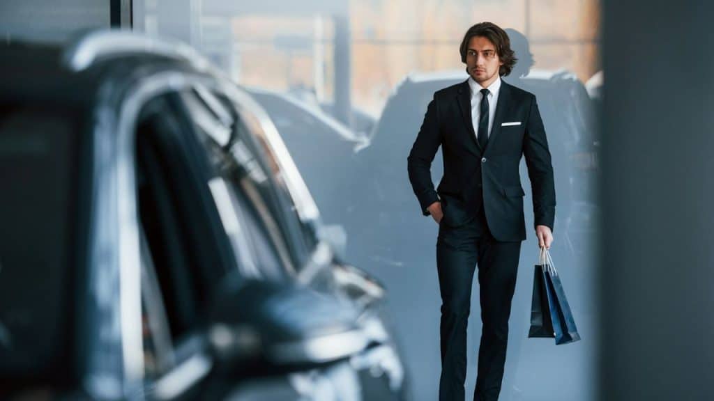 A man in a black suit with a shopping bag walks in a showroom, looking to the side.