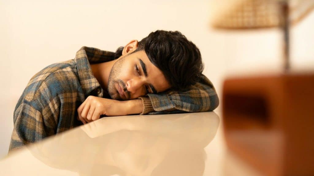 A man in a plaid shirt rests his head on a light-colored surface, looking tired.