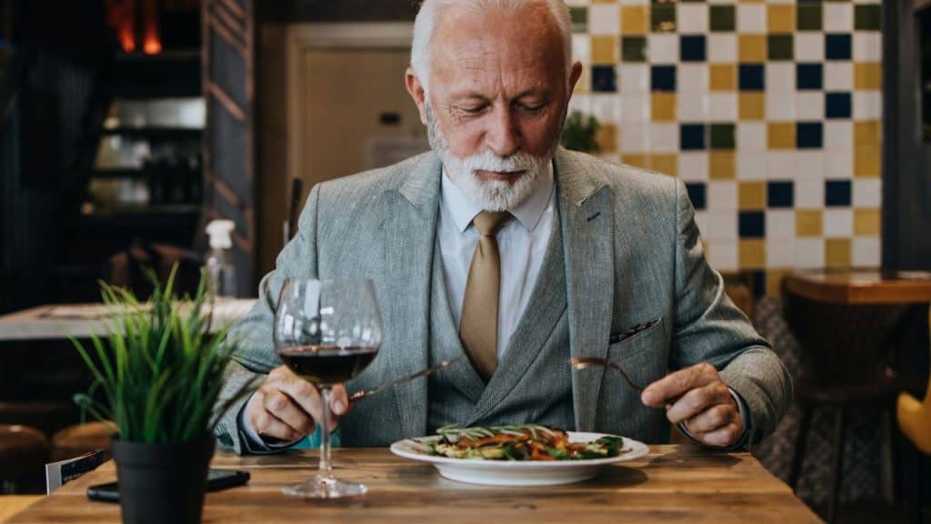 A distinguished older man with a white beard eats a meal alone.
