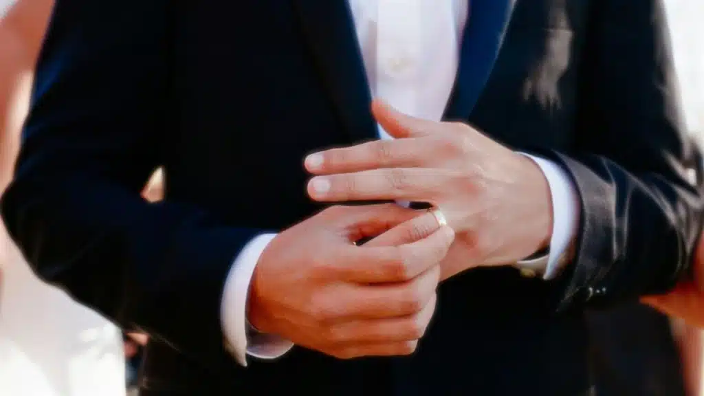 A man in a suit slides a wedding ring onto his left ring finger.