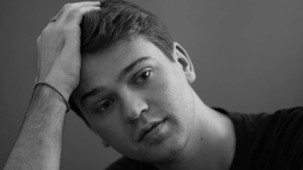 A black and white close-up of a man with his hand on his head, looking forward.
