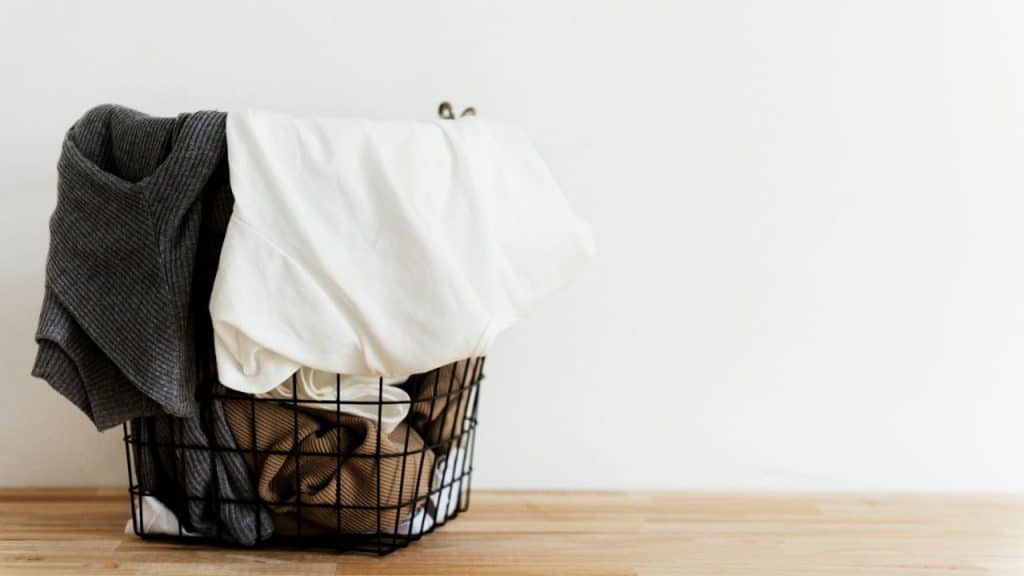 A black wire laundry basket overflowing with clothes on a light wooden floor.