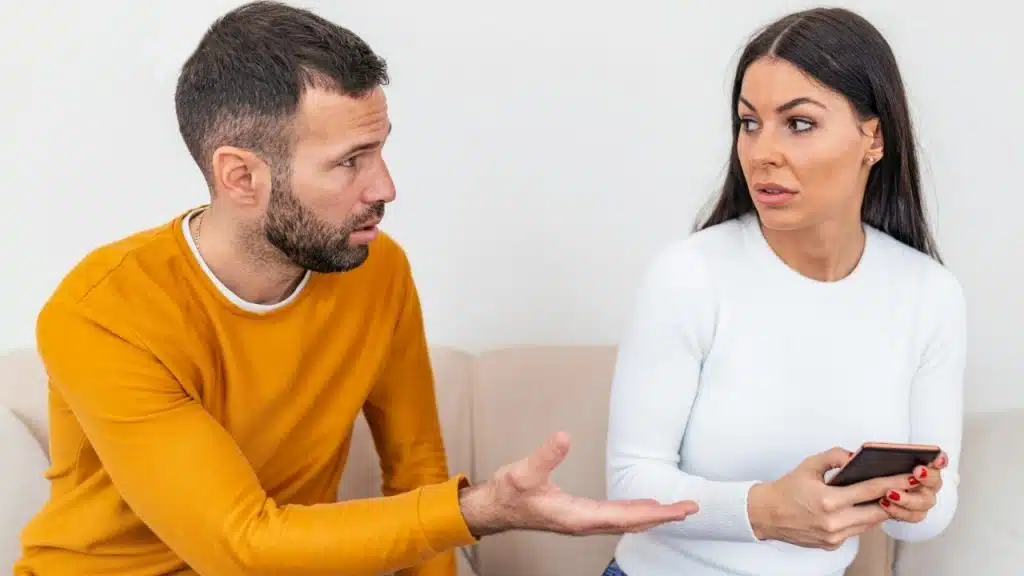 A man and woman sit on a couch, having a tense conversation.
