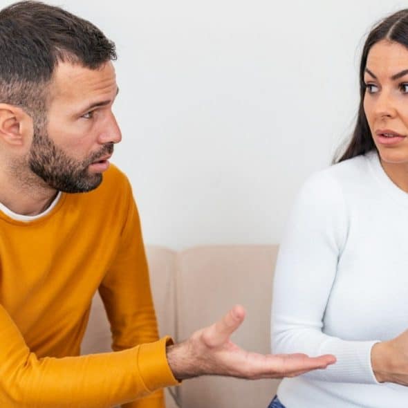 A man and woman sit on a couch, having a tense conversation.