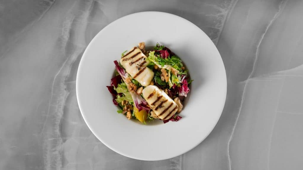 A plate of salad with grilled cheese and walnuts.