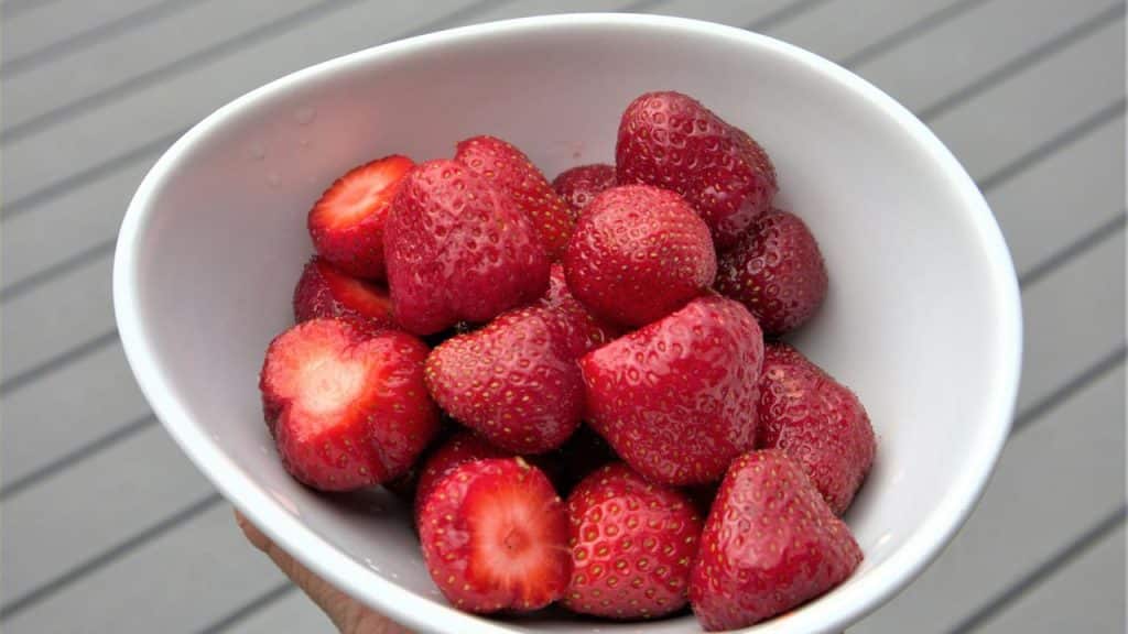 A person's hand holding a bowl of fresh strawberries.