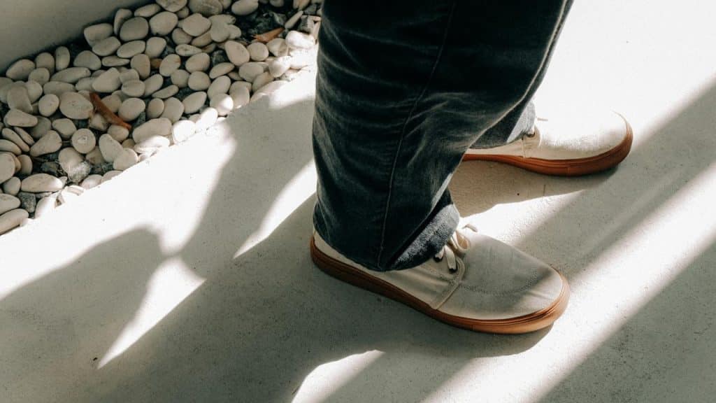 A person's legs in jeans and white shoes standing near white pebbles.