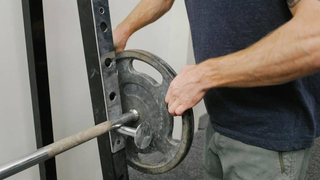 A person loading a weight plate onto a barbell in a gym.