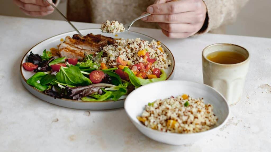 A person eating a meal with quinoa, salad, and grilled meat.
