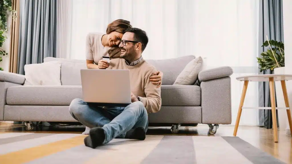 A couple in love embraces and uses a credit card or e-shopping at home