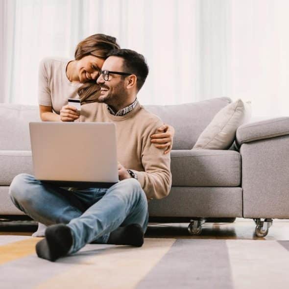 A couple in love embraces and uses a credit card or e-shopping at home