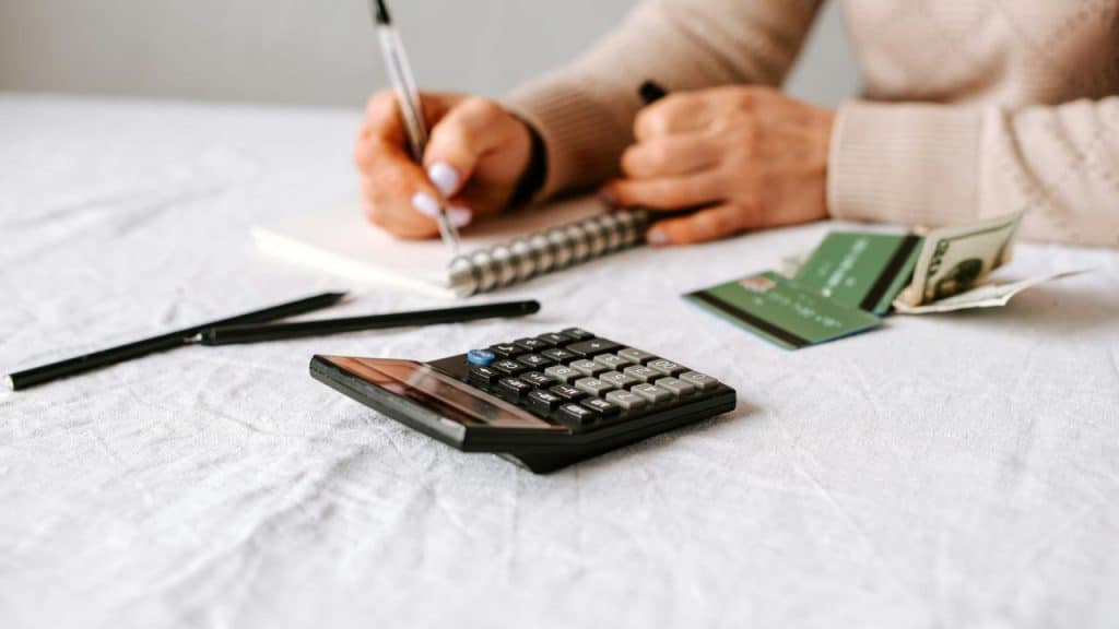 A person budgeting with a notebook, calculator, and cash.