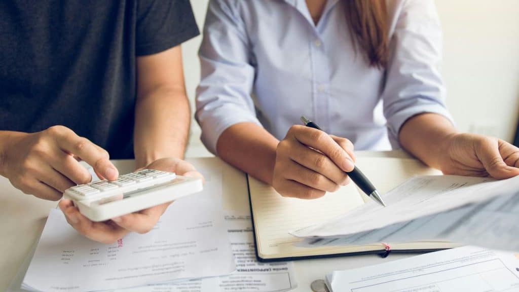 A couple calculating expenses with papers and a notebook.