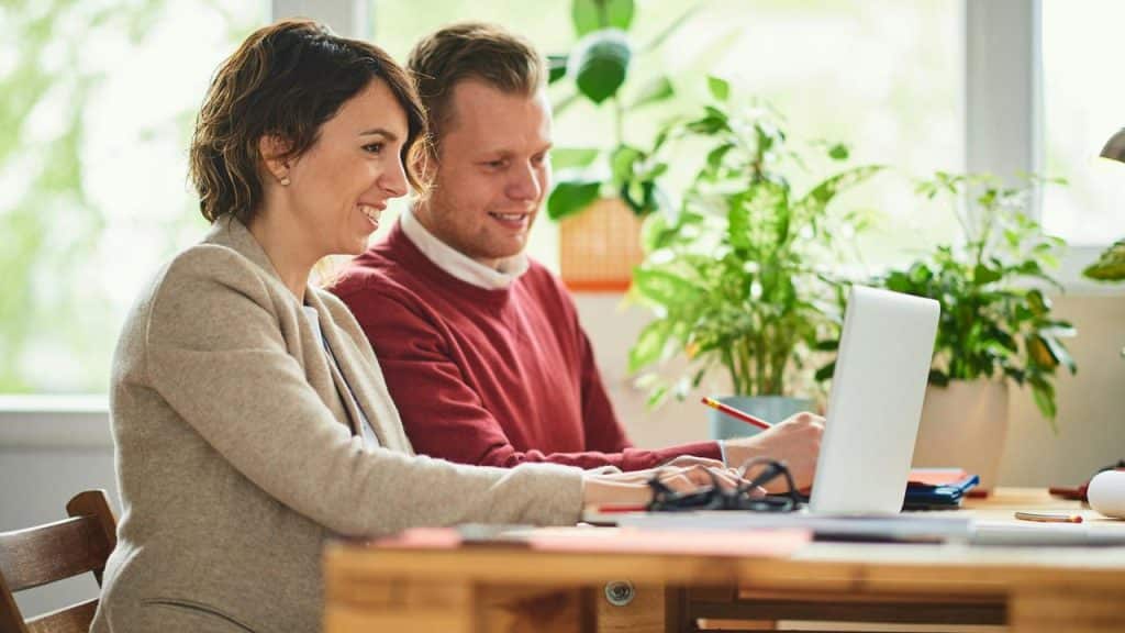 A couple smiling while working on a laptop together.