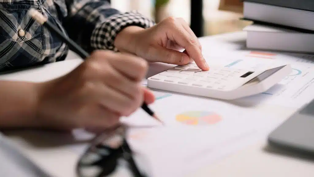 A person calculating finances with charts and a calculator.