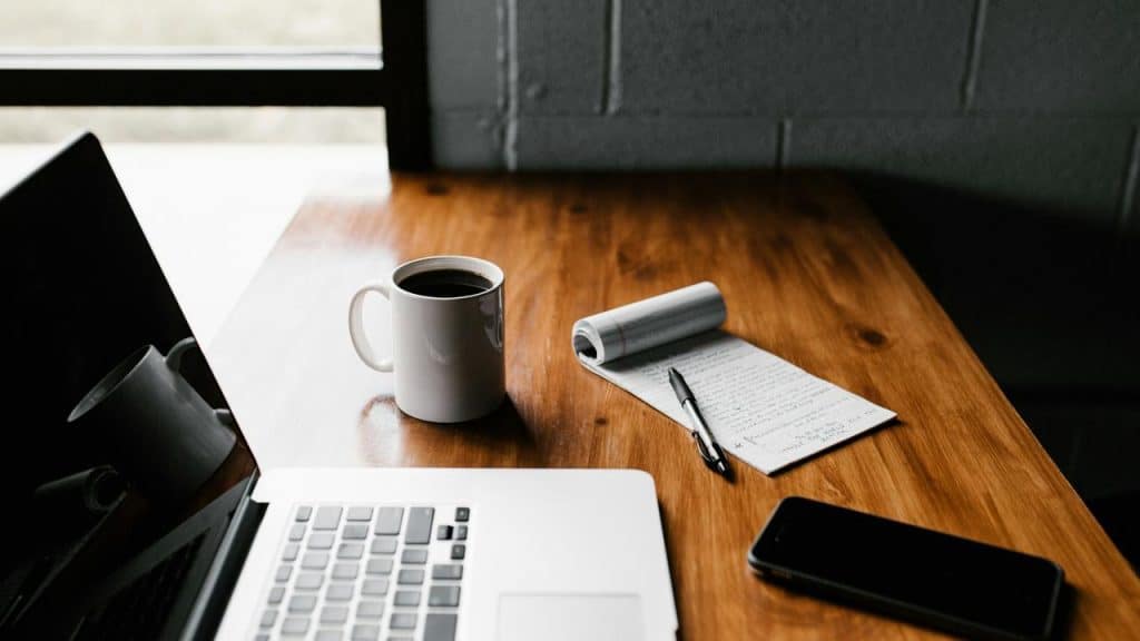 A workspace with a laptop, coffee, notepad, and phone.