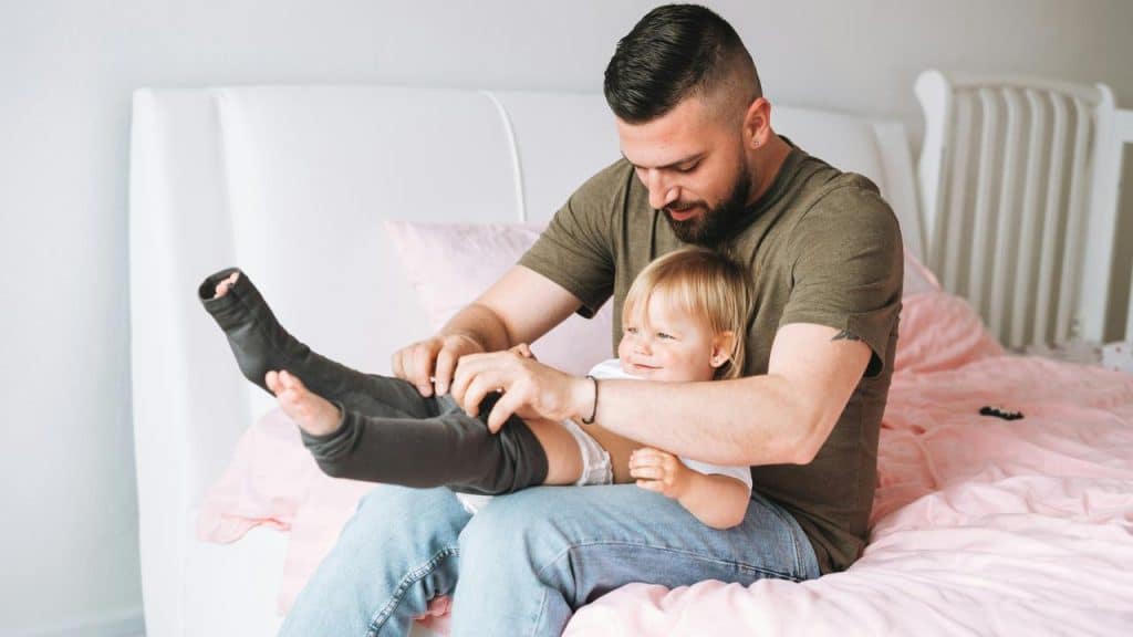 A father dresses his smiling toddler.