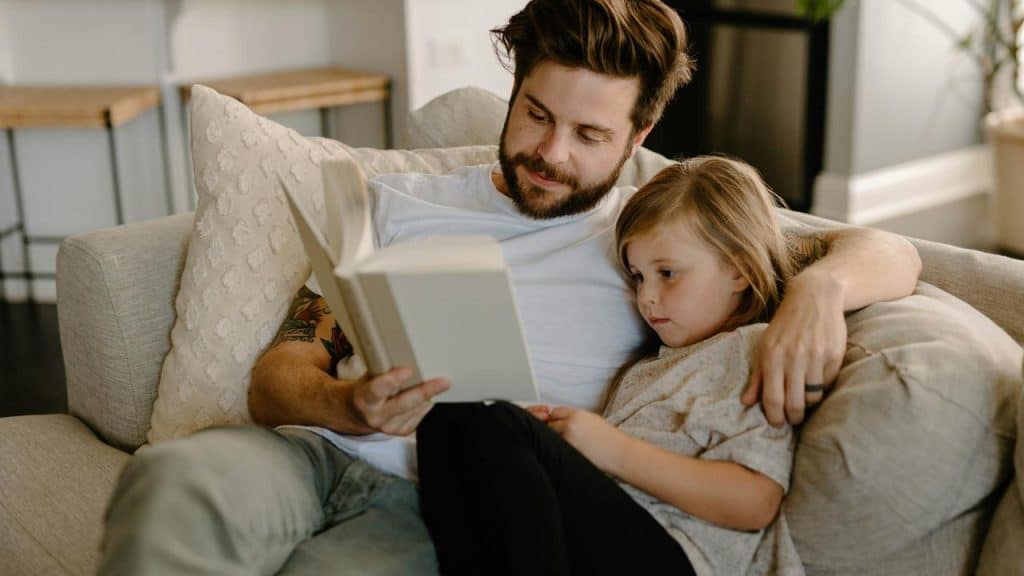 A father reads to his daughter on the couch.