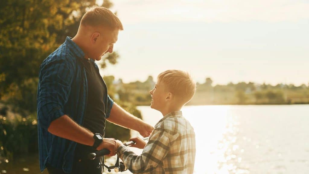 A father and son smile by a lake.