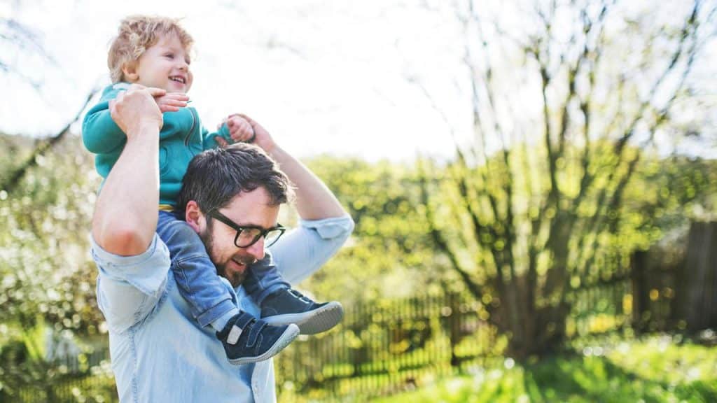 A father gives his child a shoulder ride outdoors.