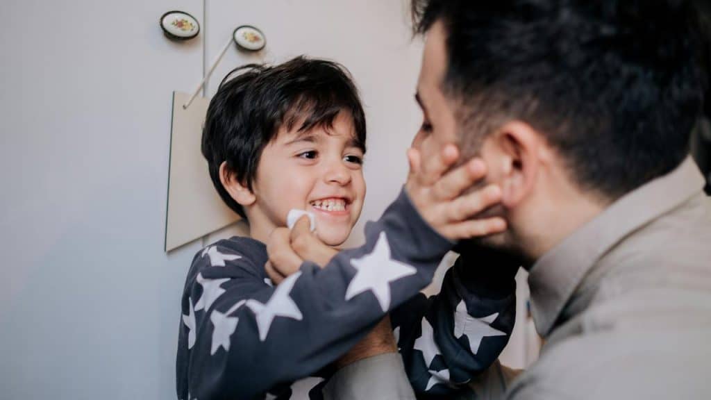 A smiling boy playfully touches his dad’s face.