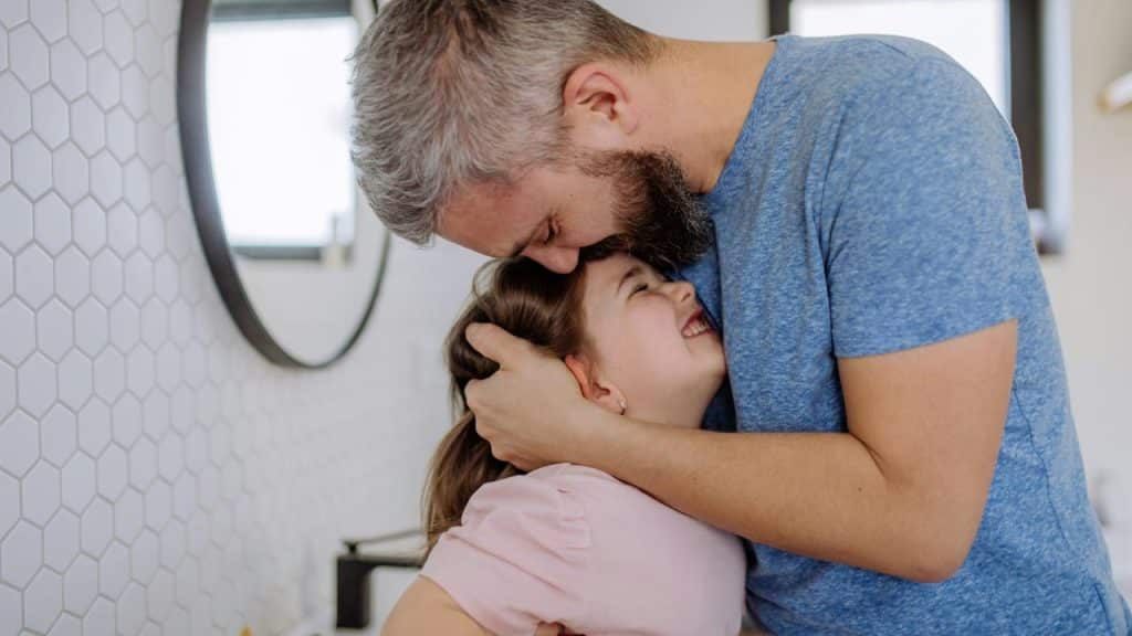 A father hugs his laughing daughter tightly.