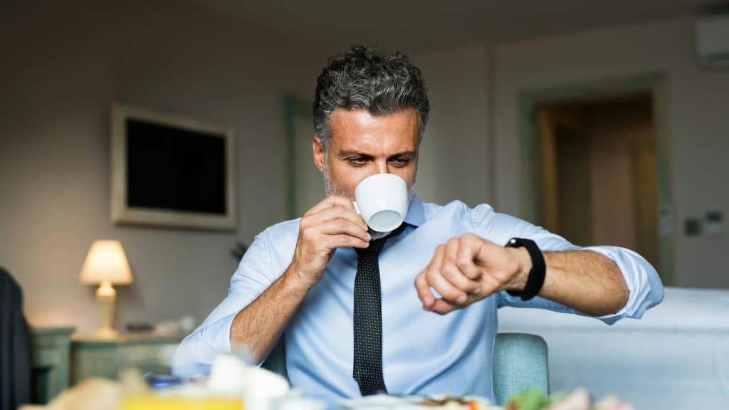 A man drinking coffee while checking his watch.
