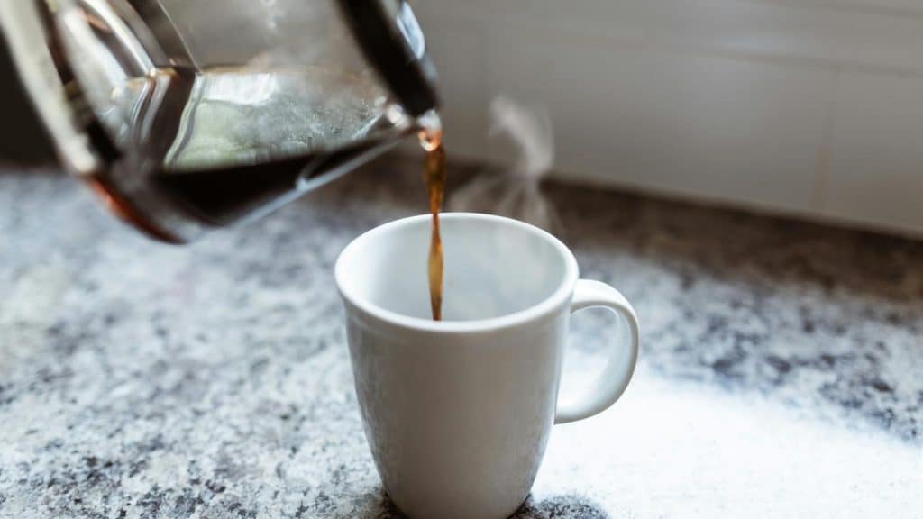 A pot pouring coffee into a white mug.