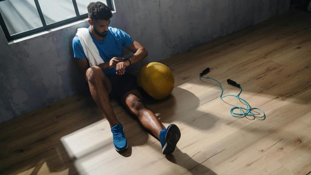 A man resting after a workout, checking his watch.
