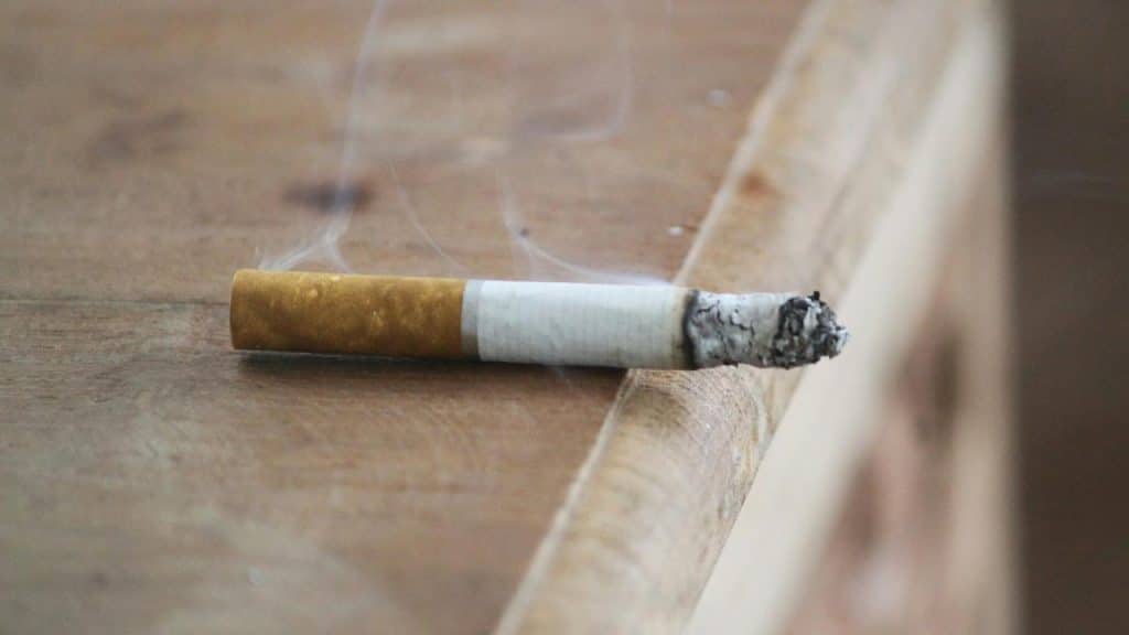A lit cigarette resting on a wooden surface.