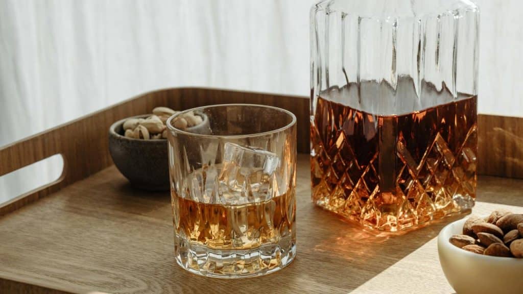 A glass and decanter of whiskey on a wooden tray.