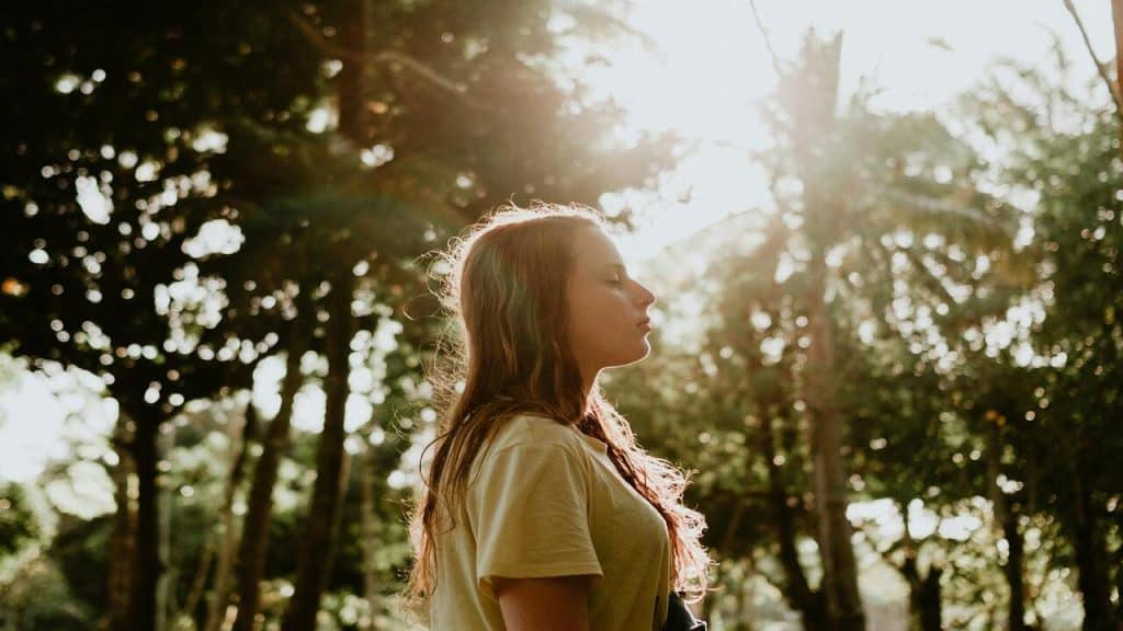 A woman taking a deep breath outdoors.