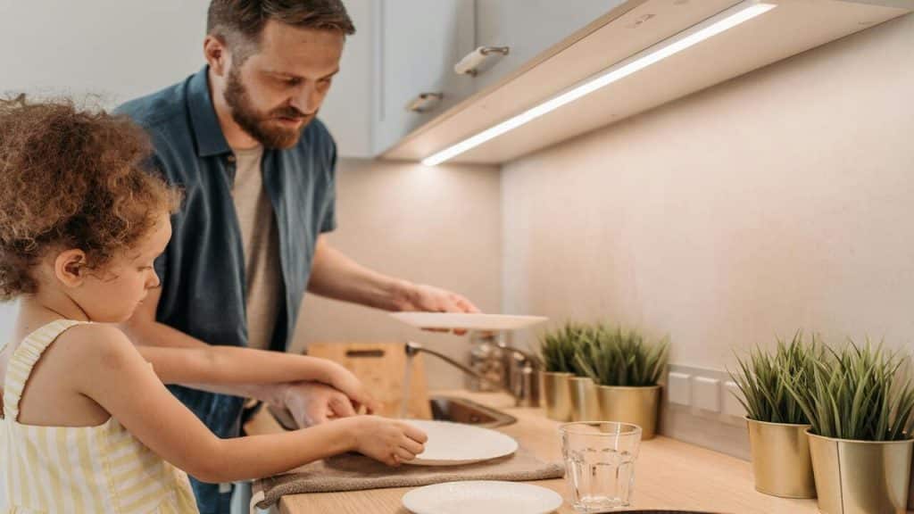 A man washing the dishes with his kid.