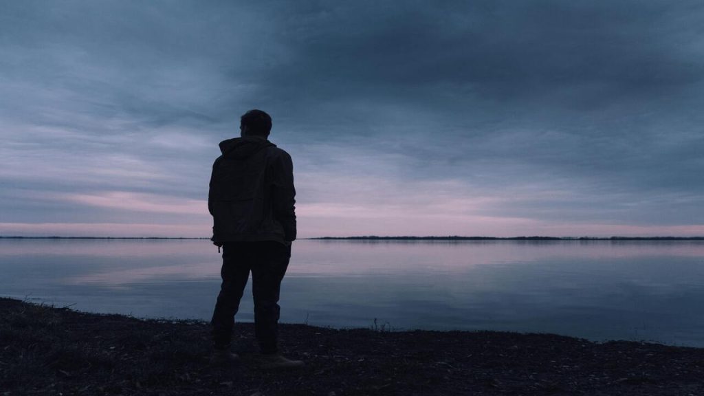 A man standing near a lake at dusk.