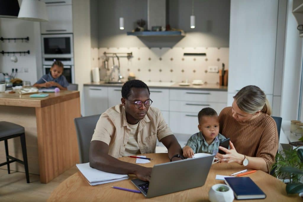 A husband busy with the laptop and a wife busy with the kids.