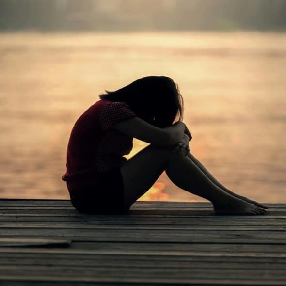 A woman looking sad by a body of water.
