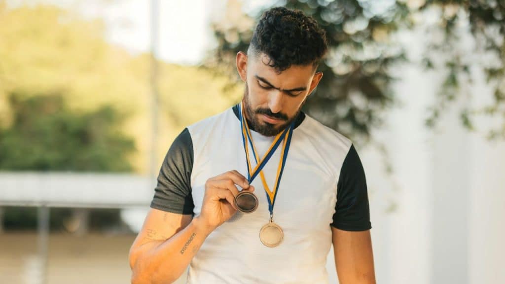 A man in a white and black shirt looks down at a medal hanging from his neck.