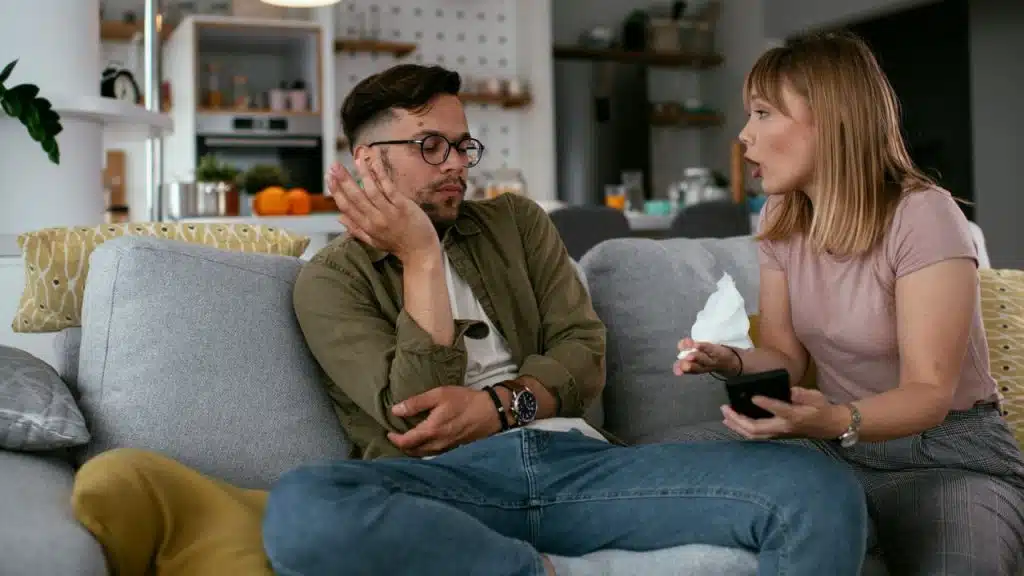 A man dismisses a woman's concerns while she holds a tissue and her phone.